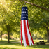 An American flag windsock hanging from a tree branch in a sunny park with green grass and trees in the background.